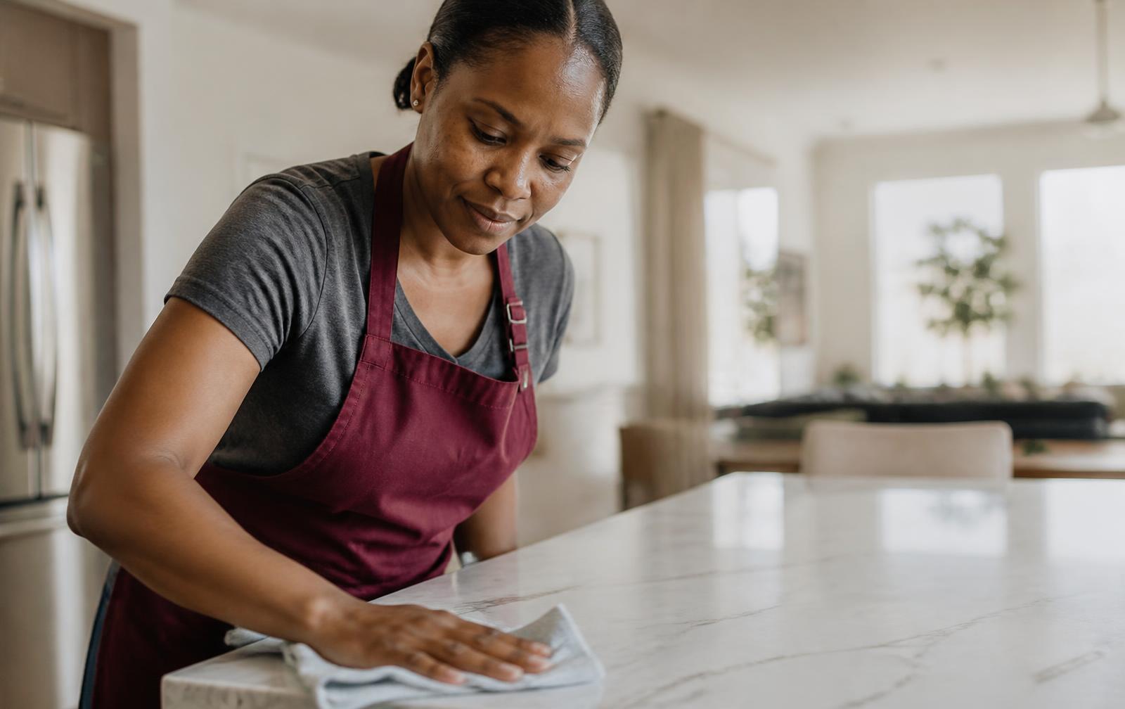 Cleaner wiping down a marble kitchen counter in a bright family home
