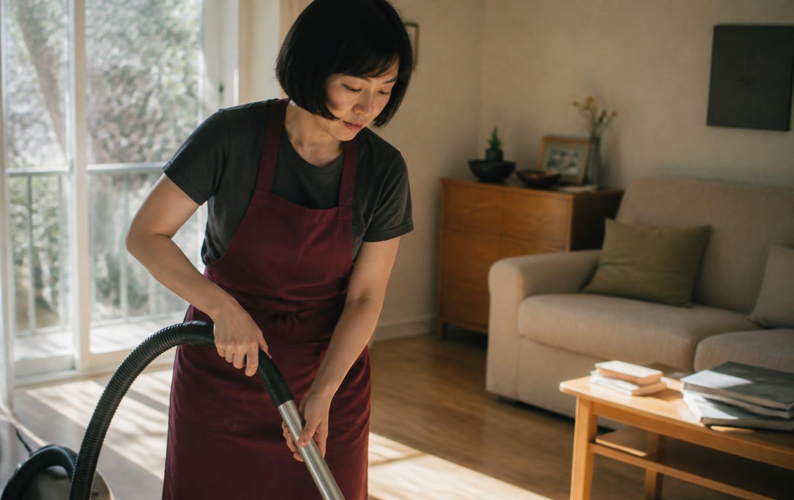 Cleaner vacuuming an oak floor in a sunlit living room